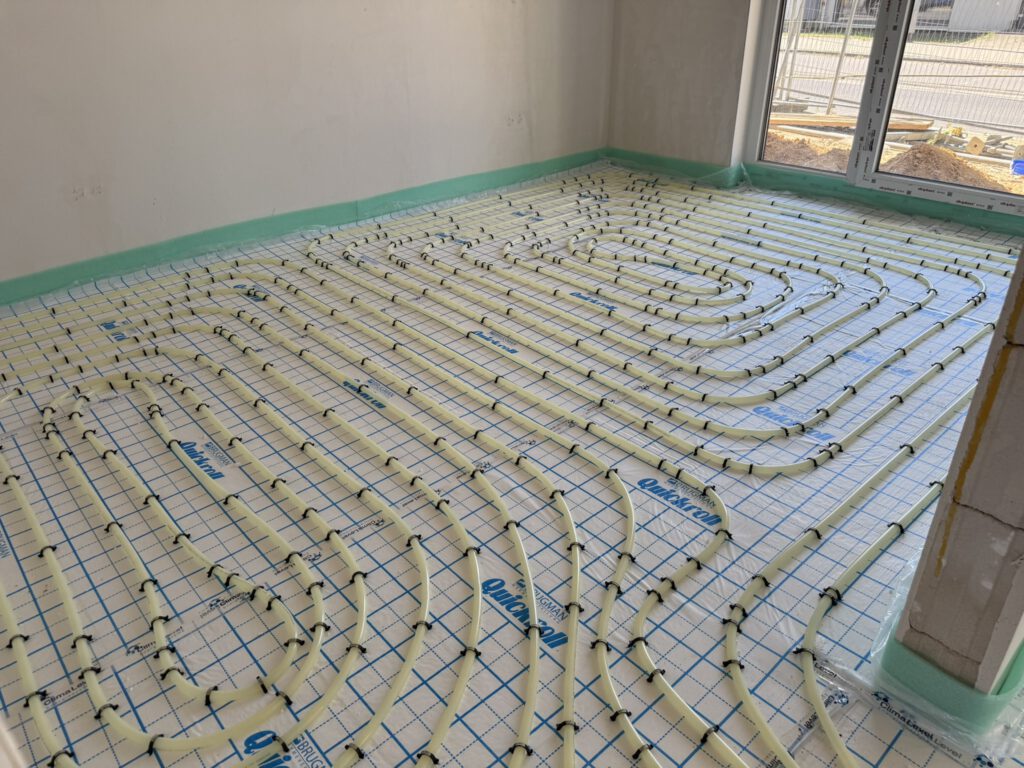 In einem Raum eines Neubaus sind die Heizungsrohre einer Fußbodenheizung in Schleifen verlegt.