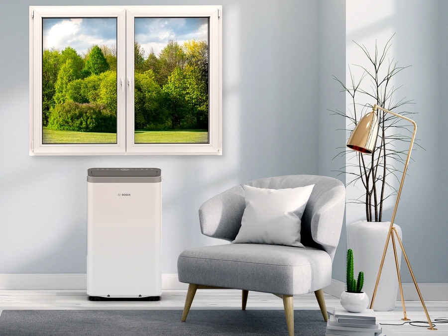 Mobile Klimaanlage von Bosch steht in einem hellen, modernen Wohnzimmer vor einem Fenster mit Blick ins Grüne