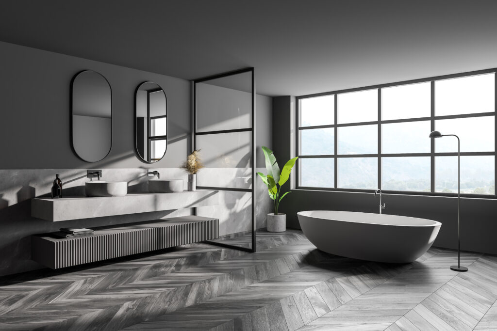 Badsanierung, Modernes Badezimmer mit freistehender Badewanne, großen Fenstern, Doppelwaschbecken und stilvollem Fischgrät-Holzboden