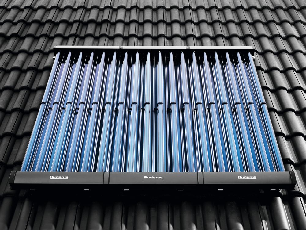 Vakuumröhrenkollektor von Buderus auf einem schwarzen Ziegeldach montiert. Die blauen Röhren sind in Reihen angeordnet und reflektieren das Licht.