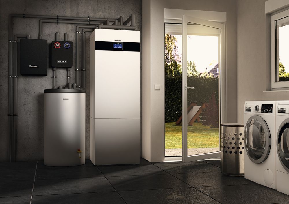 Hauswirtschaftsraum mit moderner Buderus Wärmepumpe bestehend aus mehreren Einheiten an der Wand und einem Boiler. Rechts daneben zwei Waschmaschinen und ein Wäschekorb.