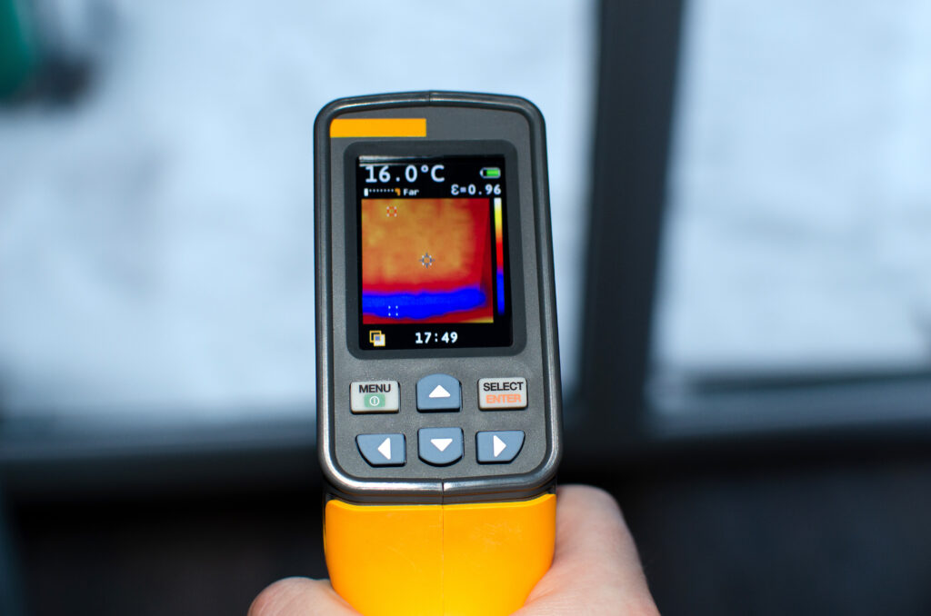 Hand hält ein Thermografiegerät mit Anzeige einer Wärmebildaufnahme und Temperatur von 16,0 °C.