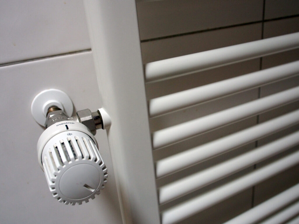 Nahaufnahme eines weißen Heizkörper-Thermostats an einem Handtuchheizkörper im Badezimmer.
